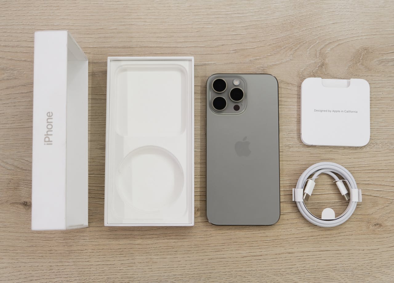 Home Flat lay view of the newest Apple iPhone model, box, and charging accessories on a wooden table.
